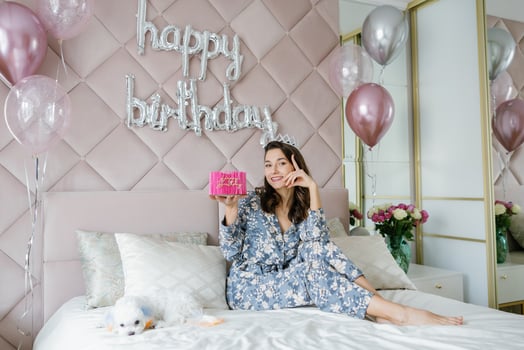 Young woman celebrating birthday with cake and balloons on bed. photo