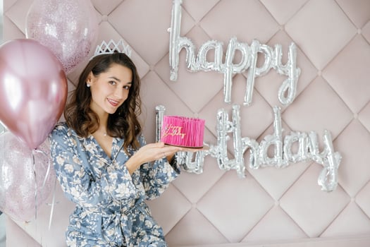 Woman celebrating birthday holding pink cake with balloons and happy birthday sign photo