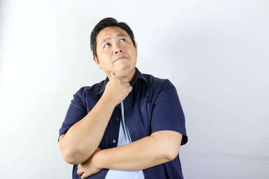 Thoughtful Asian man wearing blue t-shirt holding his chin photo