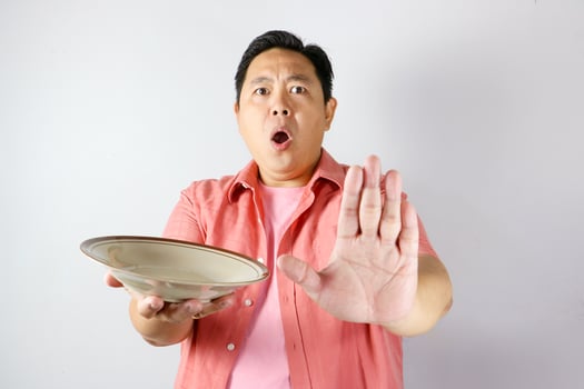 Shocked and surprised face of A man, saying no gesture wearing pink shirt holding brown empty dining plate. photo