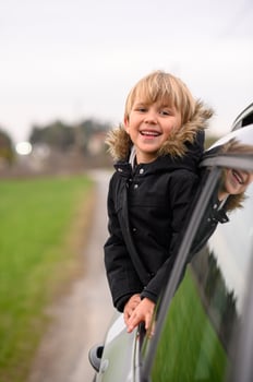 A small child embraces the thrill of the wind while riding in a car, his hair swept back by the breeze. photo