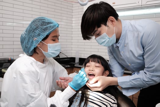 Asian female pediatric dentist examines a girl's teeth in dental clinic and takes care and encourages of father, mouth oral hygiene, and professional orthodontic healthcare work in hospital. photo