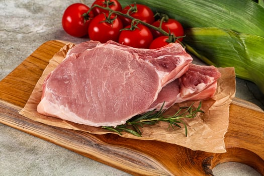 Raw pork on a cutting board with tomatoes and herbs photo