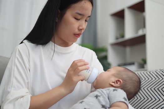 Portrait of Mother gently feeds her baby boy a bottle of milk while relaxing on a comfortable sofa in a warm living room. photo