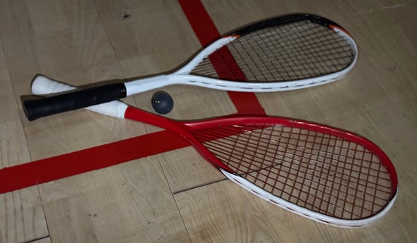 Two rackets and two squash balls lie on the parquet floor. Horizontal photo