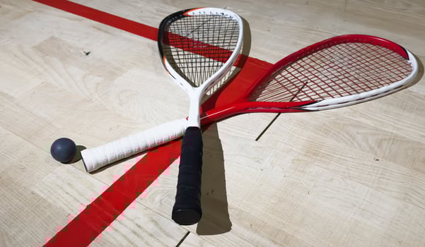 Two rackets and two squash balls lie on the parquet floor. Horizontal photo