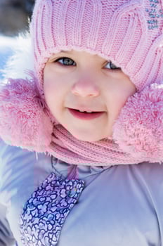 Close-up portrait of smiling girl or little child wearing pink knitted hat with pompoms photo