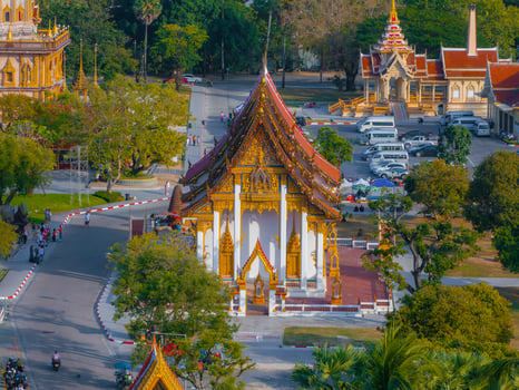 Wat Chalong in Phuket, Thailand, features ornate golden details, a steeply sloped roof, lush greenery, and visitors exploring the temple grounds. photo