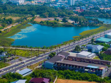 Aerial view of a lotus pond surrounded by greenery, with nearby roads, red and blue rooftops, urban structures, and lush vegetation in Phuket, Thailand. photo