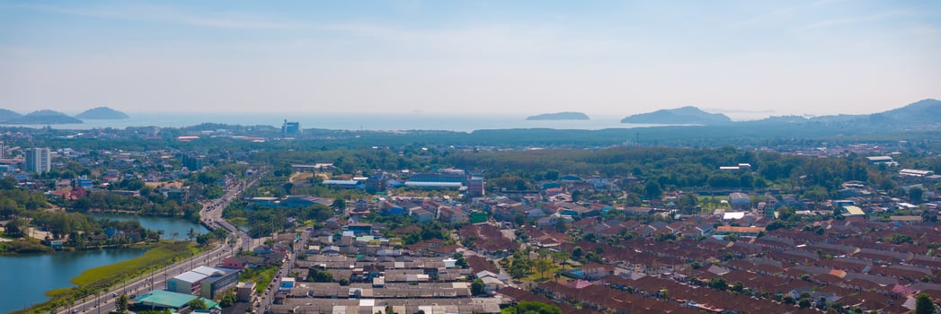Aerial view of Phuket, Thailand, showing residential neighborhoods, a small lake, roads, greenery, and the Andaman Sea with islands on the horizon. photo