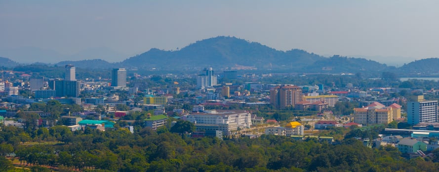 Aerial view of Phuket, Thailand, featuring modern and traditional architecture, colorful rooftops, dense greenery, and scenic rolling hills in the background. photo