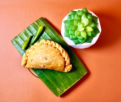 Pastel sayur with green hot chilli pepper. Deep fried Indonesian jajanan pasar dessert snacks isolated on horizontal orange brown terracota background from top angle view with cactus decoration. photo