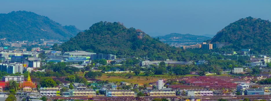 A vibrant aerial view of Phuket, Thailand, featuring a golden temple spire, colorful buildings, green hills, scattered structures, and a clear blue sky. photo