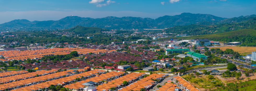 Aerial view of orange roofed houses in Phuket, Thailand, with lush green hills, the Big Buddha statue, scattered buildings, and a clear blue sky. photo