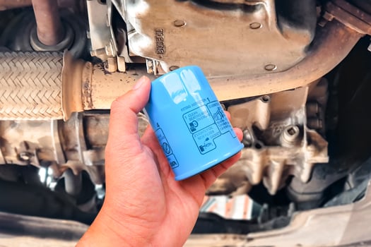 New oil filter , Hand holding blue oil filter under car engine , Car maintenance concept photo