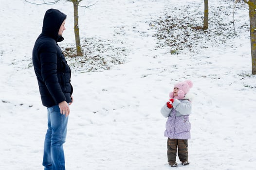 Child smiles at dad and makes snowball from snow. Father plays snowballs with little child or girl or daughter. Family games with snow in winter outside photo