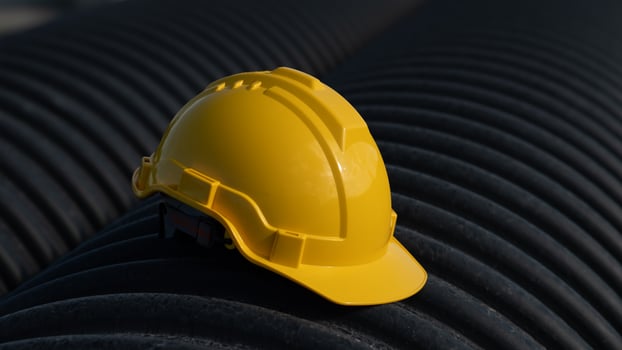A yellow hard hat sits on top of a black pipe photo