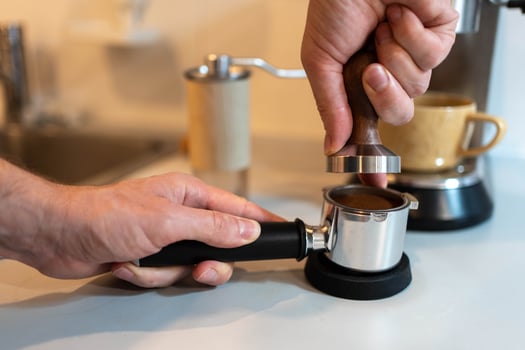 A barista carefully tamping ground coffee into a portafilter photo
