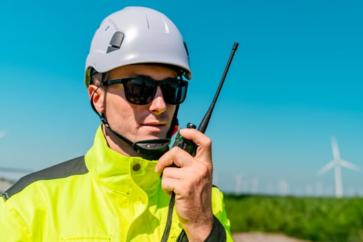 Worker in safety gear using a radio near wind turbines on a sunny day photo