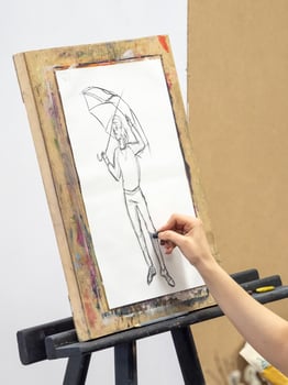 Artist's hand with a black chalk is brought to a white canvas and begins to draw a sketch. photo