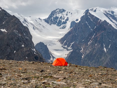 alpine landscape with vivid orange tent at very high altitude with view to high mountain and large glacier in dramatic clouds. Awesome mountain scenery with tent. photo