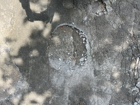 A grey concrete surface with a hole in the middle. The hole is surrounded by gravel and dir photo