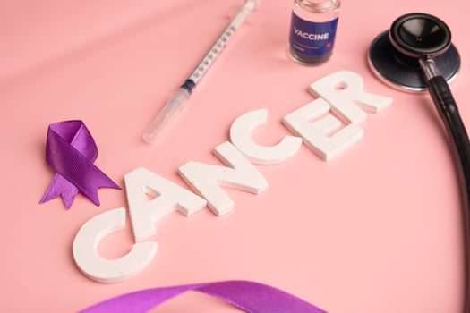 The word CANCER is spelled out with white letters alongside a purple ribbon a syringe a vaccine vial and a stethoscope. photo