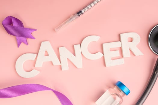 The word cancer is spelled out with white letters surrounded by a purple ribbon a syringe and a stethoscope photo