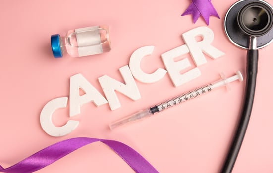 The word CANCER is spelled out with white letters next to a syringe a vial a stethoscope and purple ribbons. World cancer day photo