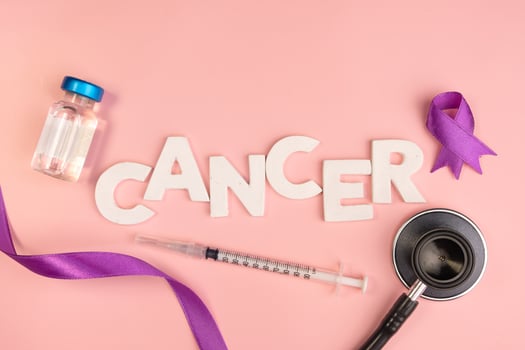 The word cancer is spelled out with white letters next to a vial syringe stethoscope and purple ribbon. Cancer awareness background photo