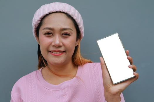 Asian woman in pink dress and beanie holding smartphone with blank white screen photo