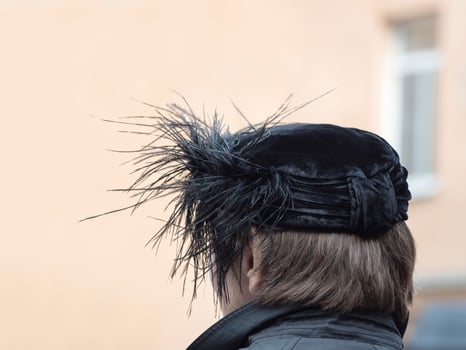 Back view of the woman with black hat with feathers on the head in a open air photo