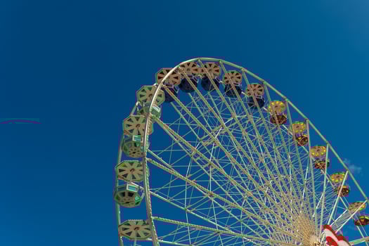 Bright ferris wheel stands against a clear blue sky at a summer fairground attracting fun seekers and families photo