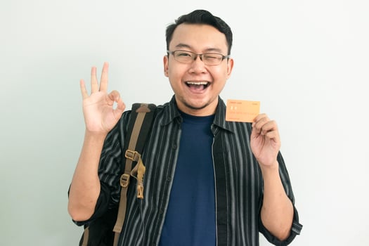 Joyful Asian Student hold credit card and doing Ok sign gesture. School, Banking, Financial isolated background, blue concept. photo