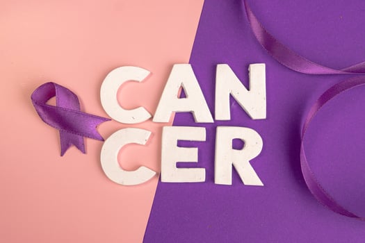 White letters spelling out cancer next to a purple ribbon. cancer awareness. world cancer day concept photo