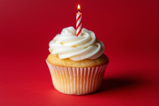 Cupcake with white frosting and red candle on a bright red background for celebration photo