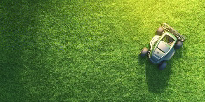 Lawn mower cutting fresh green grass during bright sunny day in outdoor garden photo