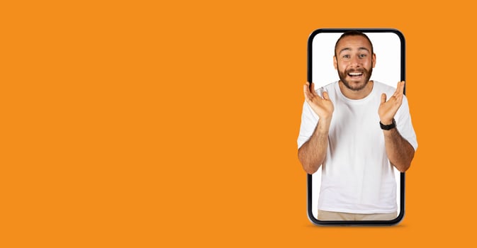 A person with a big smile is appearing to engage in lively communication through a large smartphone screen. The lively expression conveys excitement, enhancing the vibrant orange background. photo