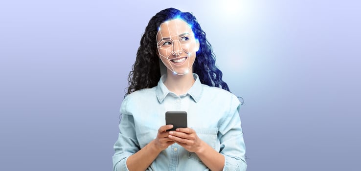 A woman with curly hair smiles while holding a smartphone. Her face is illuminated to showcase facial recognition technology, symbolizing modern identification methods in action. photo