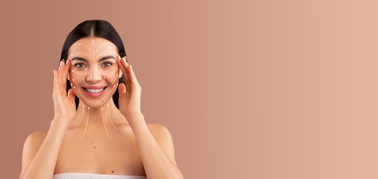 A woman enjoys a relaxing skin care routine, applying a facial treatment to enhance her beauty. She smiles while pampering herself in a peaceful setting with soft tones. photo
