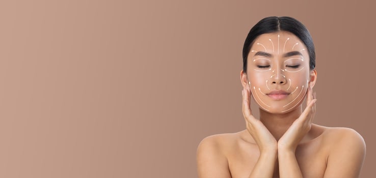 Asian woman is enjoying her skin care routine, applying techniques with her hands gently on her face. She is in a tranquil environment with a neutral background, emphasizing relaxation and pampering. photo