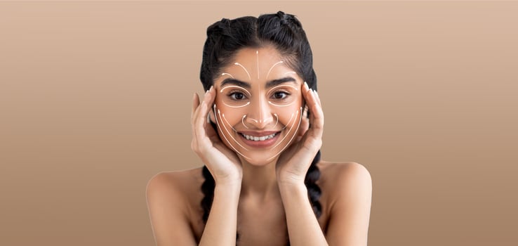 Indian woman enjoys her skin care routine, smiling and engaging in a pampering activity. She holds her face, highlighting her beauty regime in an isolated setting with soft, neutral tones. photo