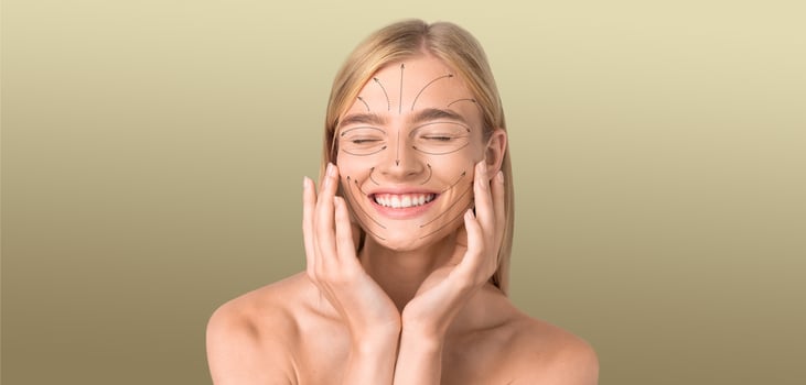 A young woman is smiling with closed eyes while applying skincare products to her face. She is in a calm, isolated environment with a smooth texture in the background, perfect for relaxation. photo