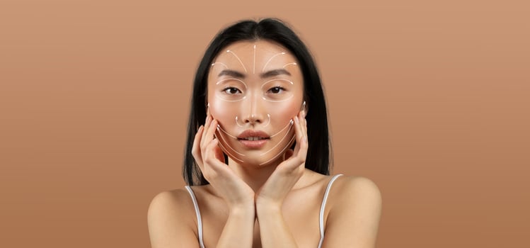 Asian woman practices her skincare routine, gently touching her face. She appears relaxed and focused, surrounded by an empty, neutral backdrop that emphasizes her beauty and self-care. photo