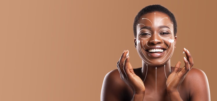 African American woman with a joyful expression is pampering her skin as part of her beauty routine. She showcases her natural glow against a warm, neutral background photo