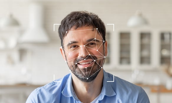 A smiling man is shown against a bright, modern kitchen background. Facial recognition technology highlights his features with geometric overlays, emphasizing identification capabilities. photo