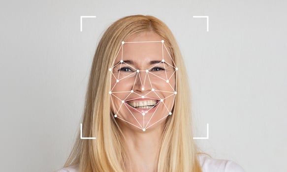 A woman with long blonde hair smiles as facial recognition technology analyzes her features. The background is a neutral color, emphasizing the focus on the subject's face and expressions. photo