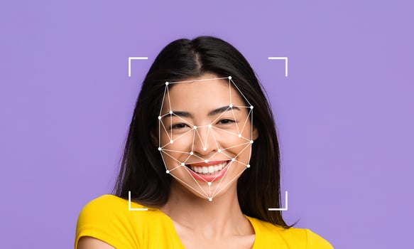 A smiling woman with long dark hair is featured in front of a purple background. Facial recognition markers are visible on her face, illustrating technology used for identification. photo