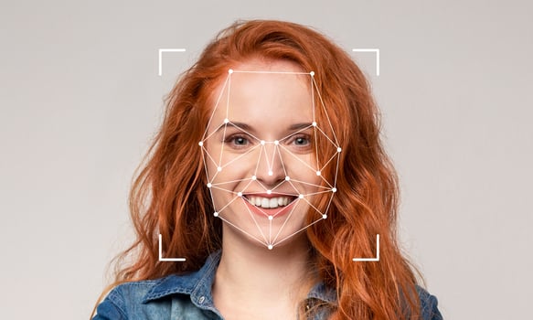 A smiling person with red hair is displayed against a plain background while facial recognition technology identifies features. The setting is neutral without specific details or distractions. photo