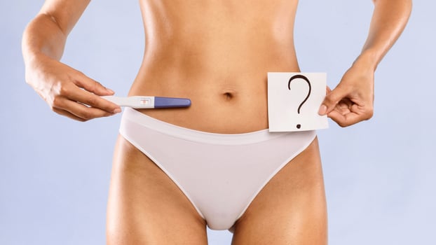 Young woman holding pregnancy test with two stripes and sticker post-it note card with question mark. Positive result. Unrecognizable female guessing unborn baby gender or thinking about abort photo